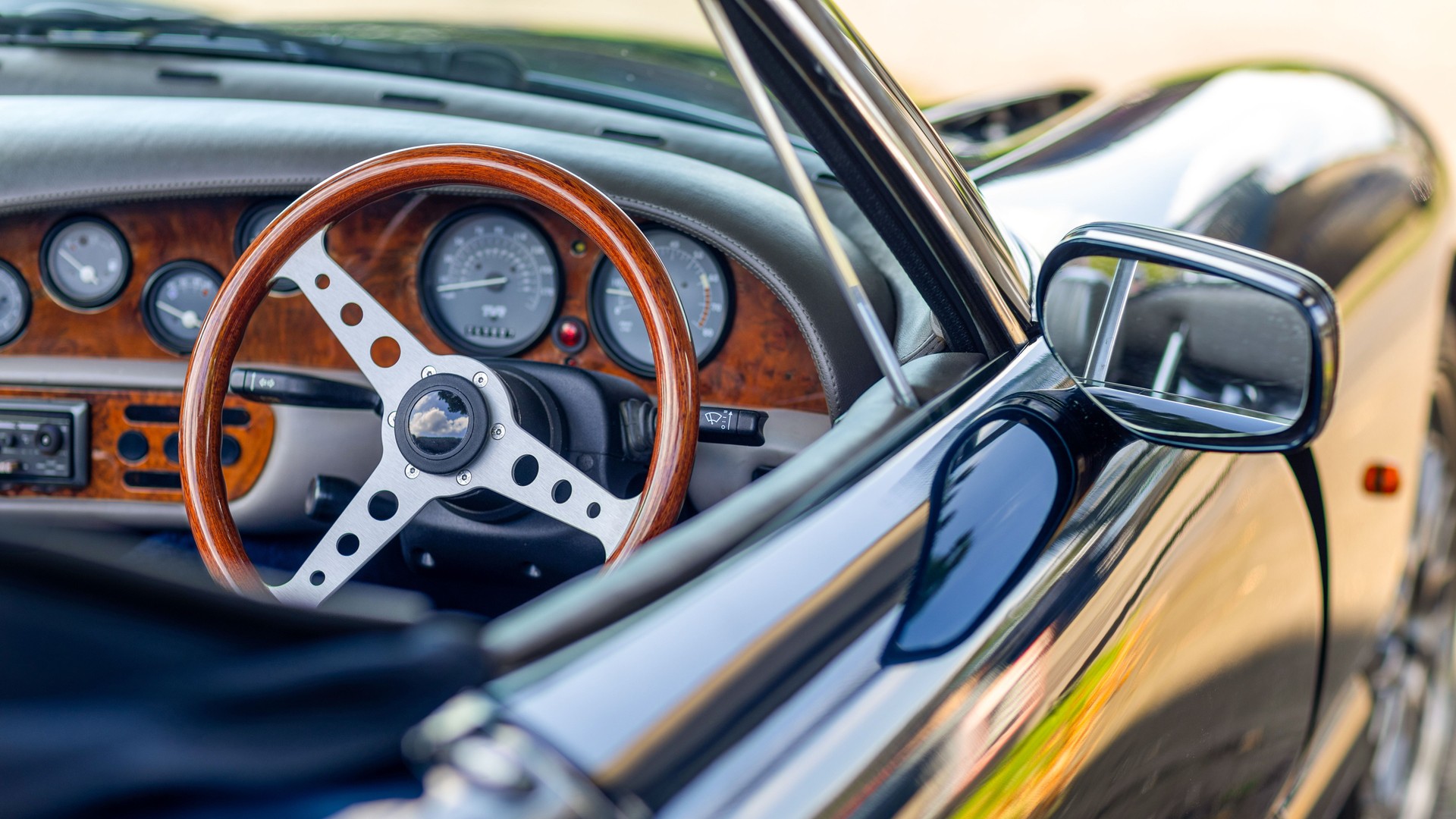 Beautiful wooden steering wheel and and old-fashioned small gauges and large beautiful exterior mirror of a historic cabriolet - right-hand drive